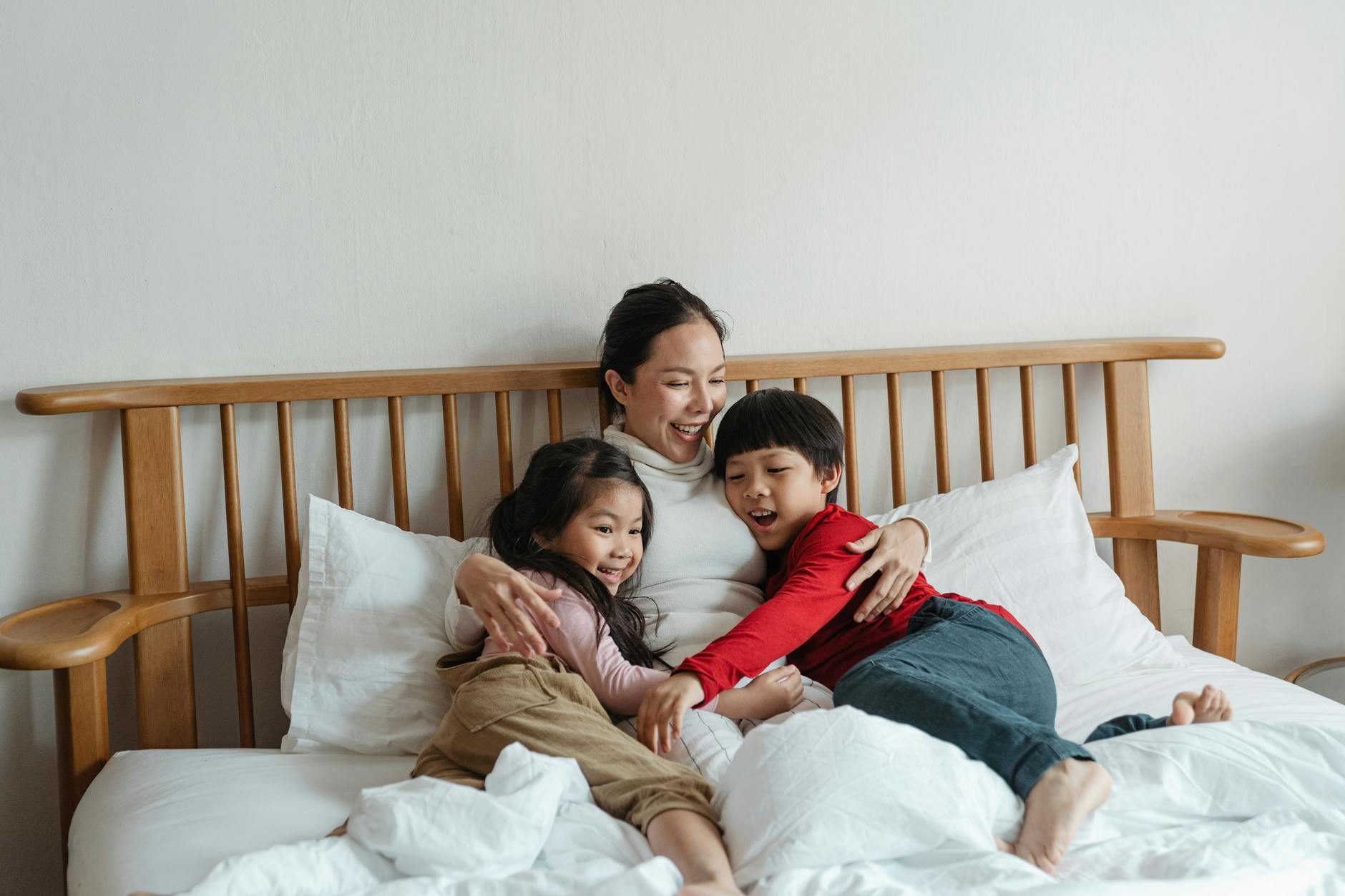 cheerful ethnic mother hugging children lying in bed family